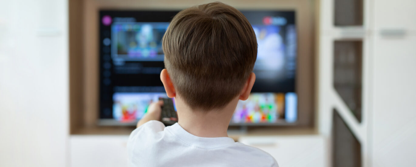 Little boy is sitting on the couch and switching TV channels.
