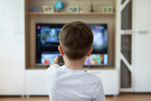 Little boy is sitting on the couch and switching TV channels.