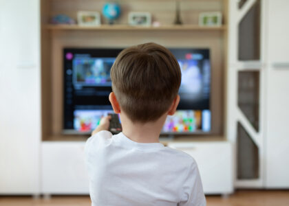Little boy is sitting on the couch and switching TV channels.